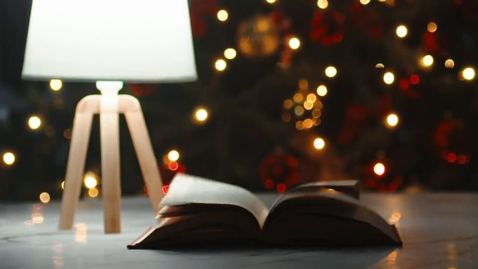 Hero film still: a white lamp glowing beside an open book