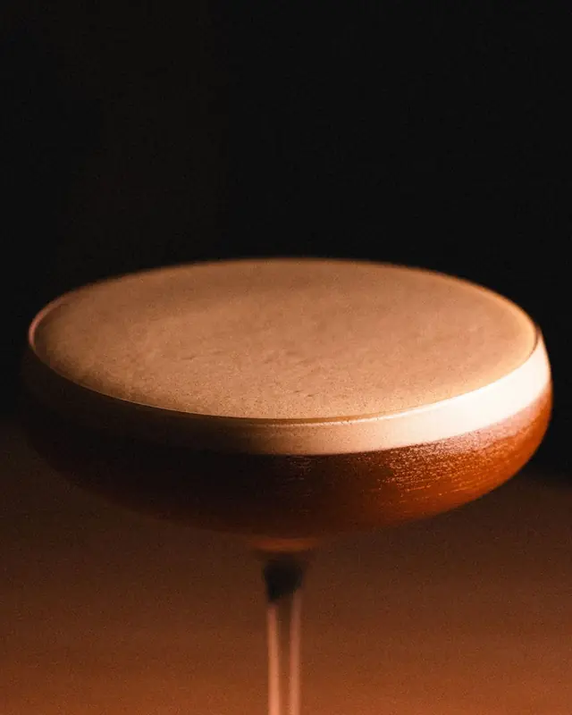 A cocktail coupe glowing amber in a dark bar
