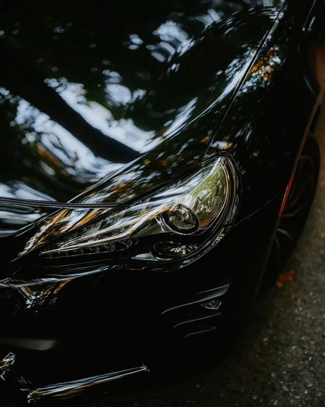 The headlight of a black car reflecting trees