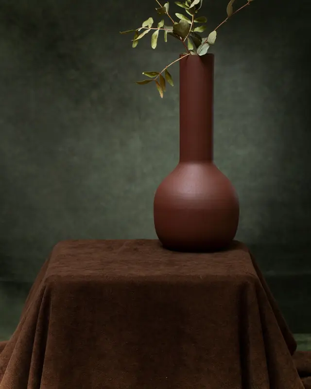 A terracotta vase on brown velvet against green